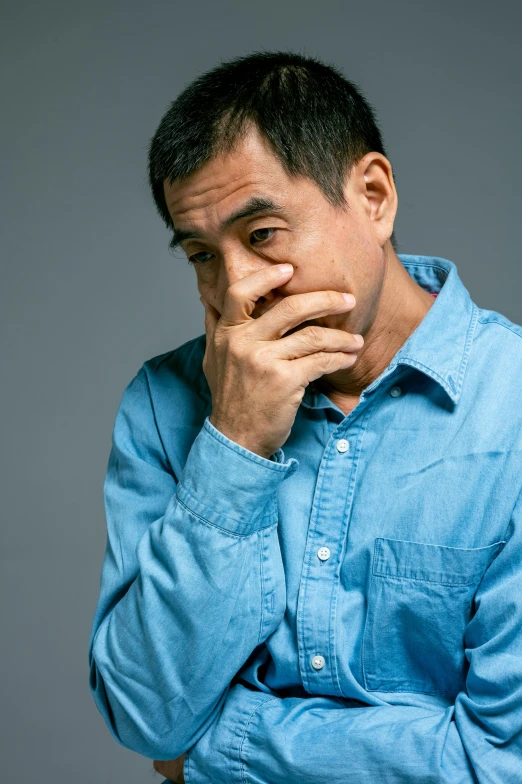 a man in a blue shirt holding his hand to his face, portrait of mr bean, asian male, pouty, david marquez