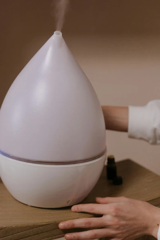 a white humider sitting on top of a wooden table, hands touching light drops, cone shaped, with accurate features, video