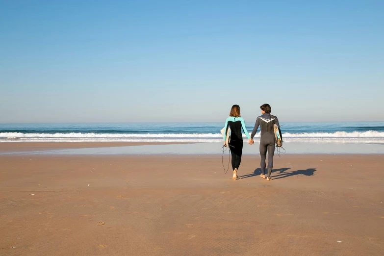 a couple of people standing on top of a sandy beach, surfing, profile image, on the beach at noonday, walking towards you