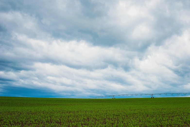 a field of green grass with a sprinkler in the distance, by Kristin Nelson, unsplash contest winner, giant clouds, minimalist photo, farms, ultrawide landscape