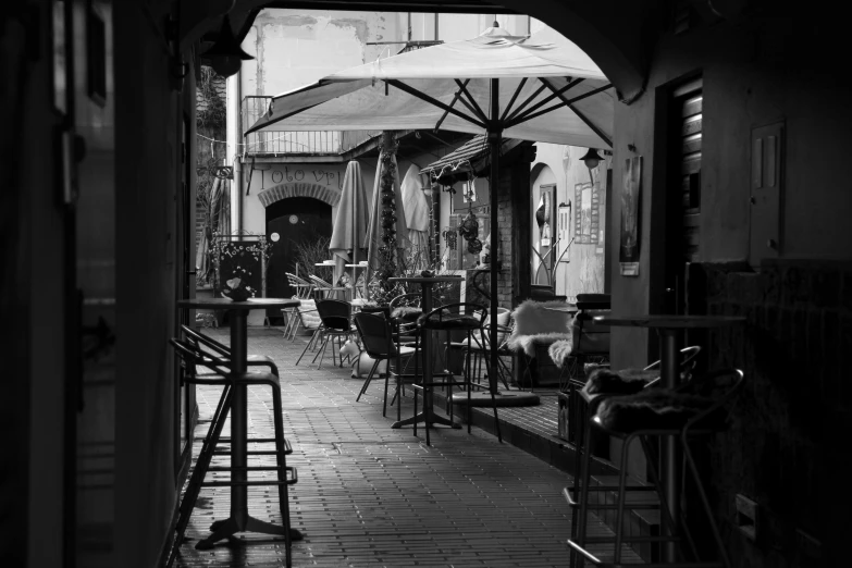 a black and white photo of an outdoor cafe, a black and white photo, pexels, process art, alley, umbrellas, interior of a small, in town