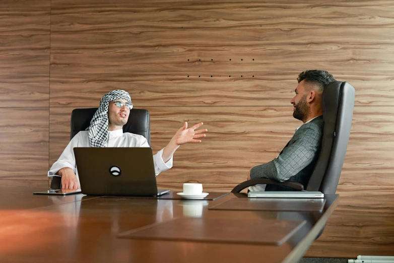 a man and a woman sitting at a table with a laptop, by Ismail Acar, pexels contest winner, hurufiyya, in a meeting room, an arab standing watching over, dressed thobe, slightly minimal