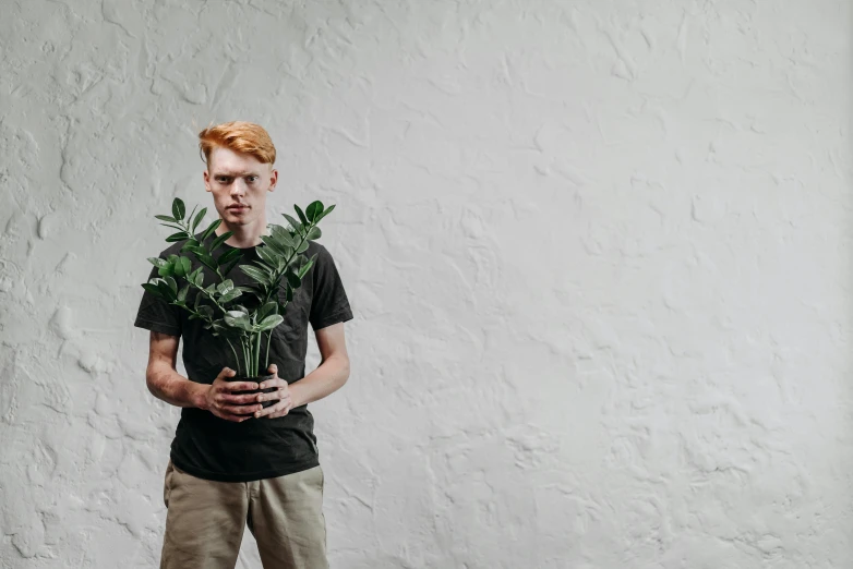 a man standing in front of a white wall holding a plant, pexels contest winner, red haired teen boy, greens), hr ginger, ignant