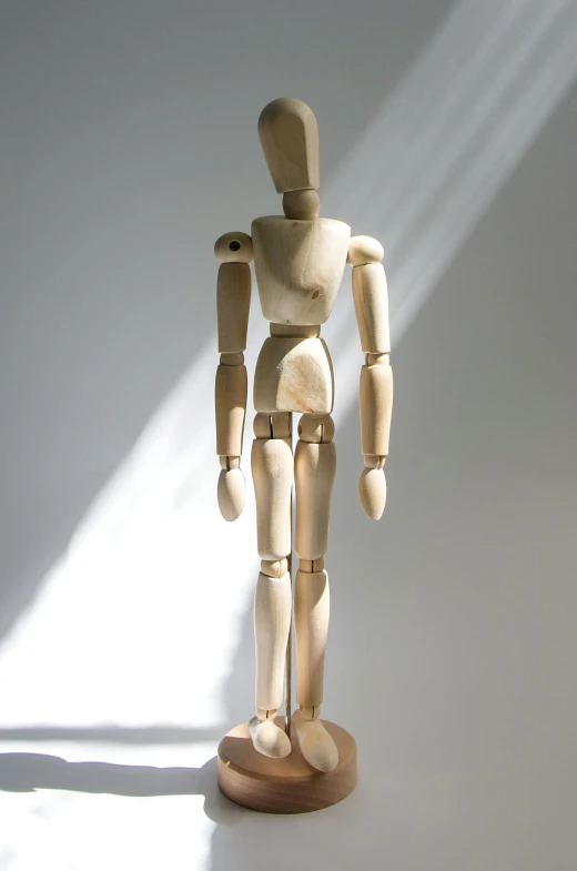 a wooden mannequin standing in front of a white wall, articulated joints, sunlight beaming down, slightly muscular, modelling