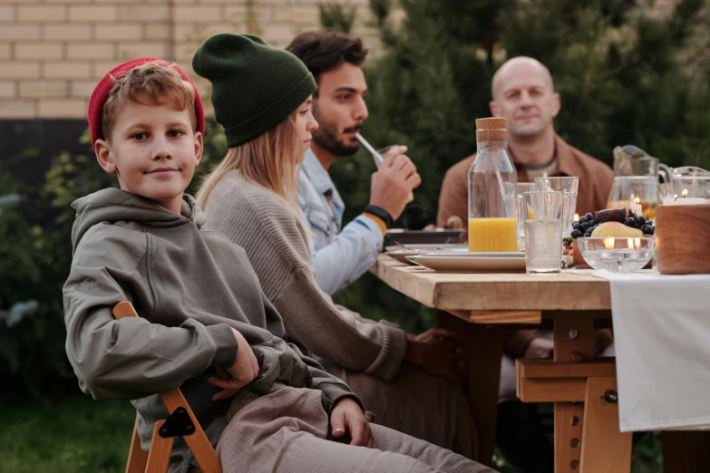 a group of people sitting around a wooden table, pexels contest winner, husband wife and son, teenager hangout spot, ecovillage, smoking outside