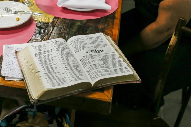 an open book sitting on top of a wooden table, religión, eating, defined, full-body