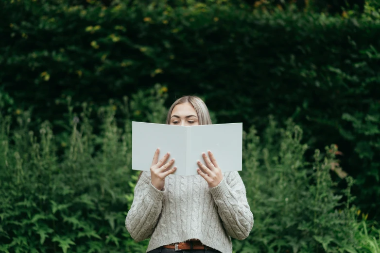 a woman sitting on a bench reading a book, pexels contest winner, standing in a grassy field, wearing a white sweater, avatar image, close-up photo