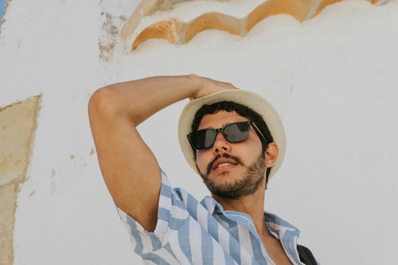 a man wearing a hat and sunglasses leaning against a wall, background image, alexandros pyromallis, upper body image, vacation photo