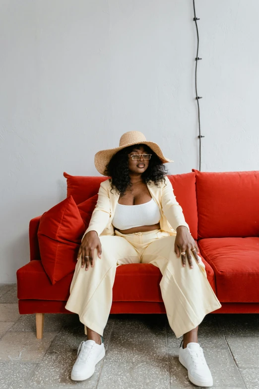 a woman sitting on top of a red couch, by Lily Delissa Joseph, pexels contest winner, afrofuturism, beige fedora, in a white boho style studio, corporate boss, thicc