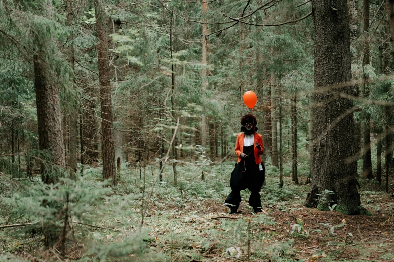 a person with an orange balloon in the woods, costume, ((forest)), looking towards the camera, black forest