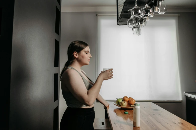 a woman standing in a kitchen holding a cup, inspired by Elsa Bleda, pexels contest winner, profile image, sitting on the table, low quality photo, thicc