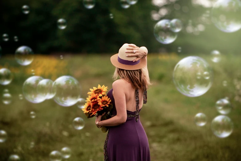 a woman standing in a field surrounded by bubbles, pixabay contest winner, bouquets, woman with hat, yellow and purple tones, shot from the back