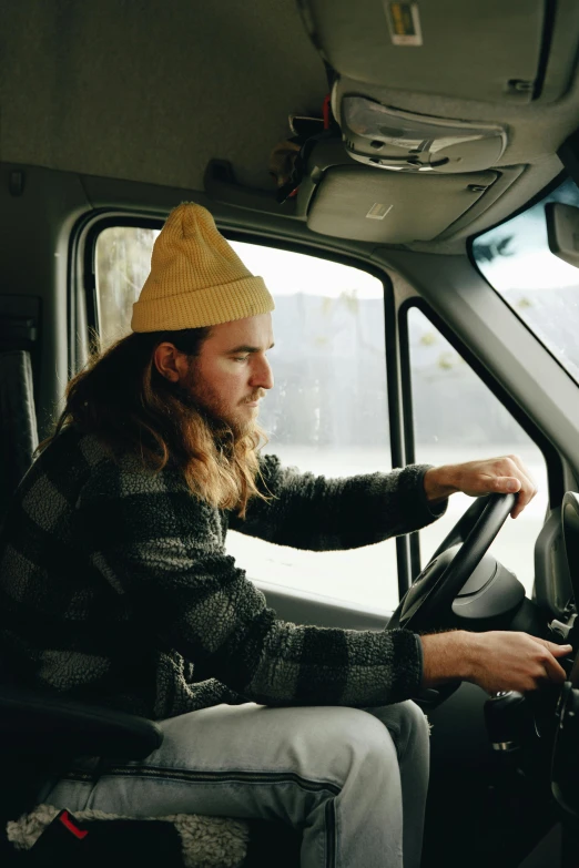 a man sitting in the driver's seat of a truck, a portrait, trending on pexels, long yellow hair, beanie, cone, standing sideways