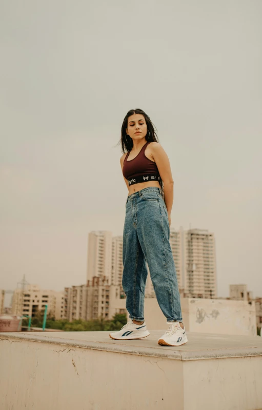 a woman standing on a ledge with buildings in the background, trending on pexels, graffiti, croptop, indian, 90s photo, jeans pants