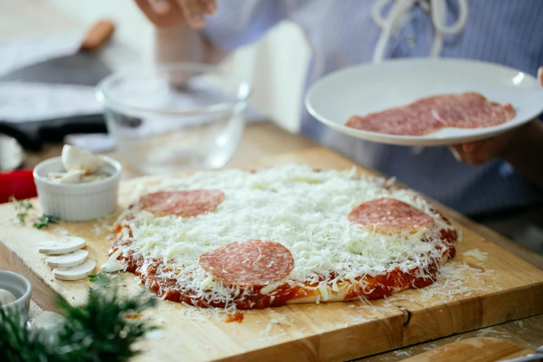 a pizza sitting on top of a wooden cutting board, by Julia Pishtar, cheese and salami on the table, holiday season, family friendly, on kitchen table