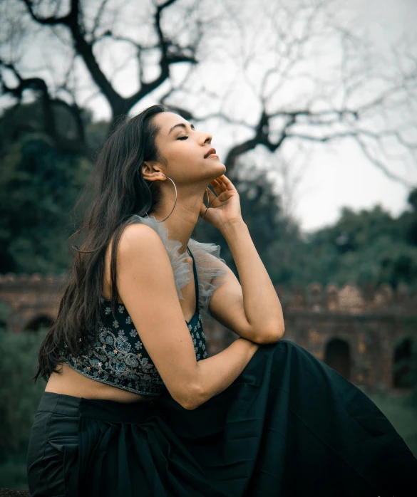 a woman sitting on top of a lush green field, an album cover, pexels contest winner, black jewellery, candid!! dark background, in a city park, profile posing