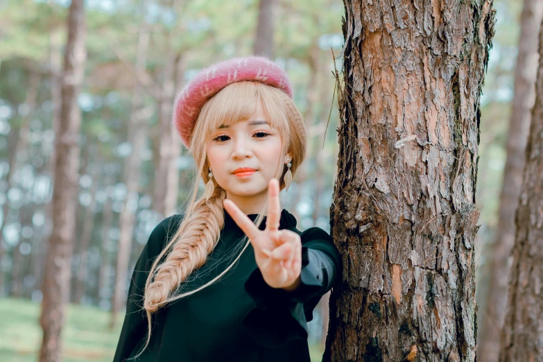 a woman standing next to a tree in a forest, an album cover, inspired by Kim Jeong-hui, unsplash, realism, blond hair with pigtails, black beret, young cute wan asian face, peace sign