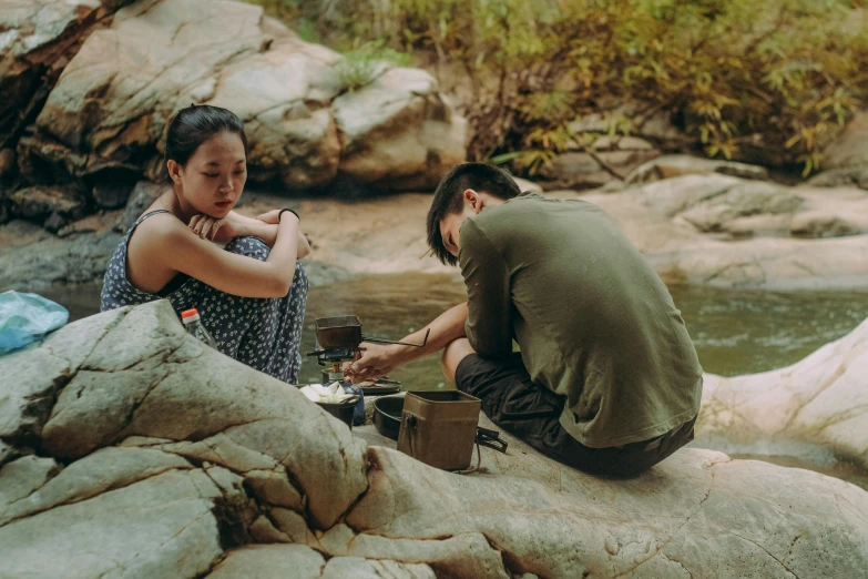 a couple of people sitting on top of a rock next to a river, pexels contest winner, korean woman, hot food, scene from the film, collaborative