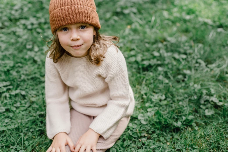 a little girl sitting on top of a lush green field, inspired by Kate Greenaway, pexels contest winner, wearing beanie, cinnamon skin color, wearing casual sweater, manuka