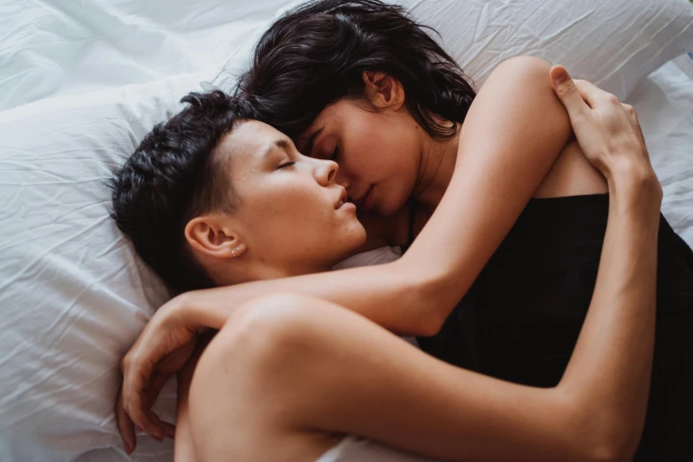 a couple laying on top of a bed next to each other, by Julia Pishtar, trending on pexels, romanticism, asian female, gay, holding each other, asleep