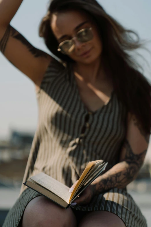 a woman sitting on a bench reading a book, pexels contest winner, happening, arms covered in gang tattoo, holding books, up close shot, sun overhead