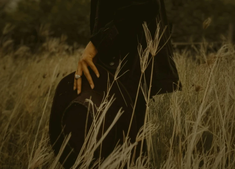 a woman standing in a field holding a hat, an album cover, pexels contest winner, dark and muted colors, sleek hands, kneeling, dark. no text
