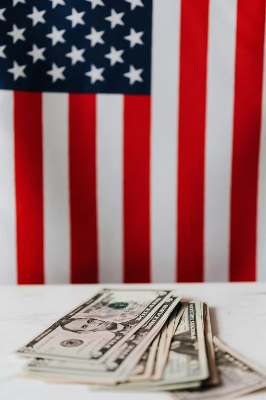 a stack of money sitting on top of a table next to an american flag, a portrait, pexels contest winner, instagram post, conservative, multiple stories, 🚿🗝📝