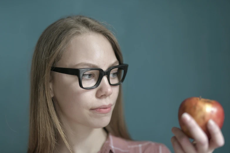 a woman in glasses is holding an apple, by Adam Marczyński, trending on pexels, hyperrealism, avatar image, cinematic still frame, low quality photo, people look into the frame