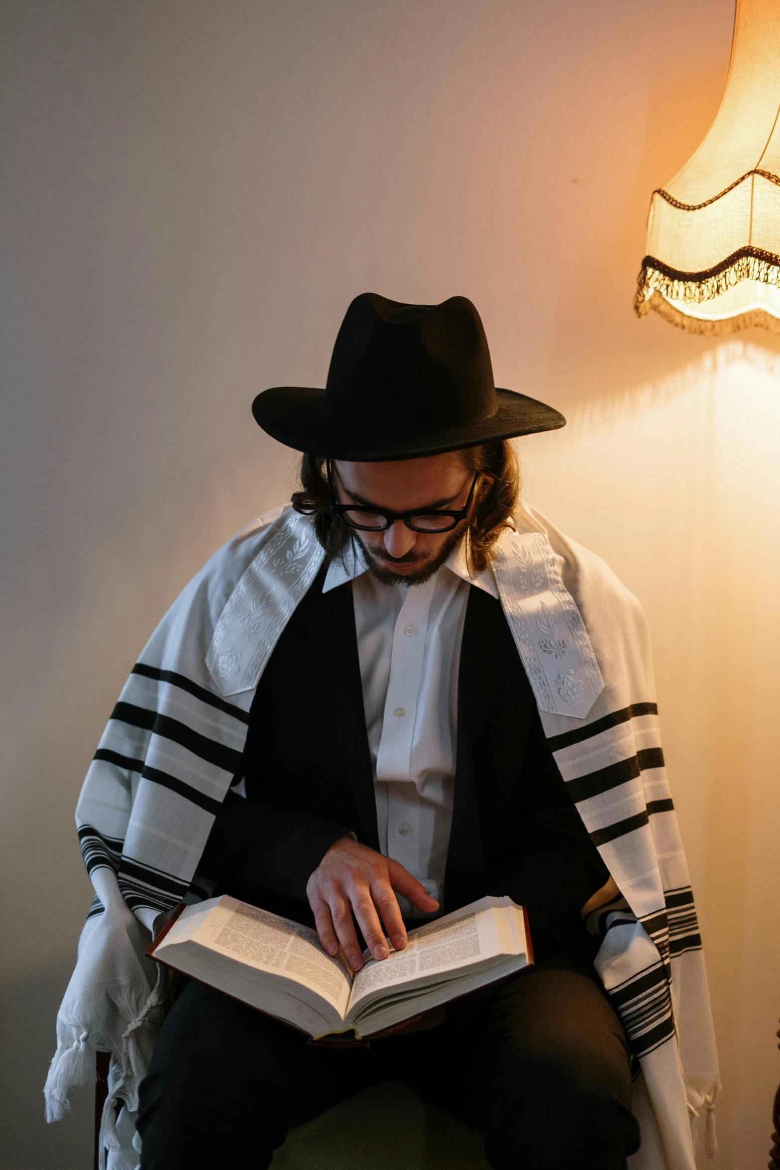 a man sitting in a chair reading a book, by Emanuel Witz, trending on unsplash, sukkot, ferred - themed robes and hat, he is casting a lighting spell, jewish young man with glasses