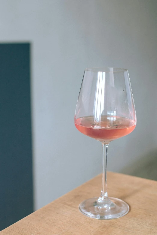 a wine glass sitting on top of a wooden table, by Jan Wijnants, pink rosa, standing sideways, zoomed in, lightweight