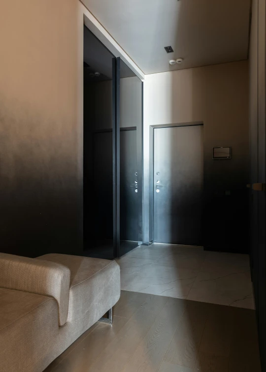 a white couch sitting in a living room next to a doorway, a picture, by Adam Marczyński, unsplash, in an elevator, ombre, charcoal and silver color scheme, exiting from a wardrobe