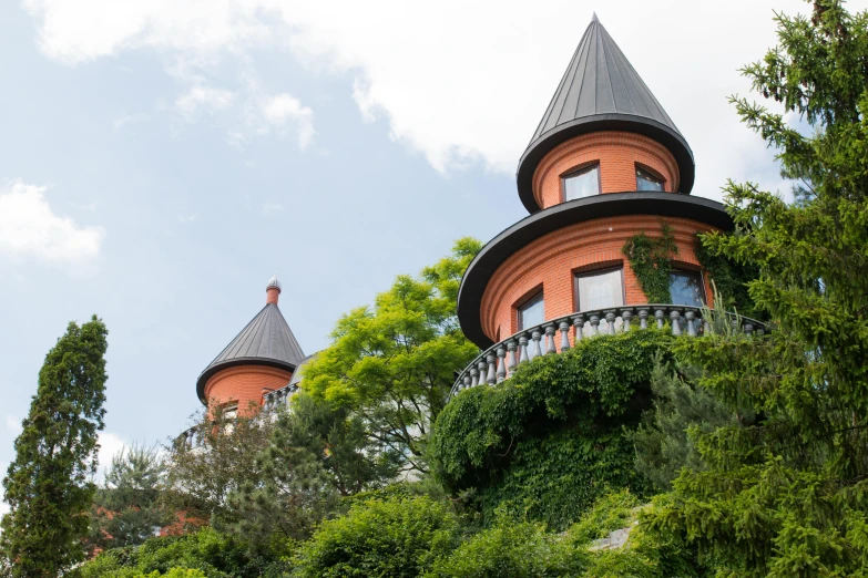 a red building sitting on top of a lush green hillside, a photo, by Adam Marczyński, art nouveau, two organic looking towers, castelvania, rounded roof, espoo