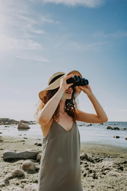 a woman standing on a beach looking through a pair of binoculars, trending on pexels, wearing a travel hat, al fresco, humans exploring, wearing an eyepatch