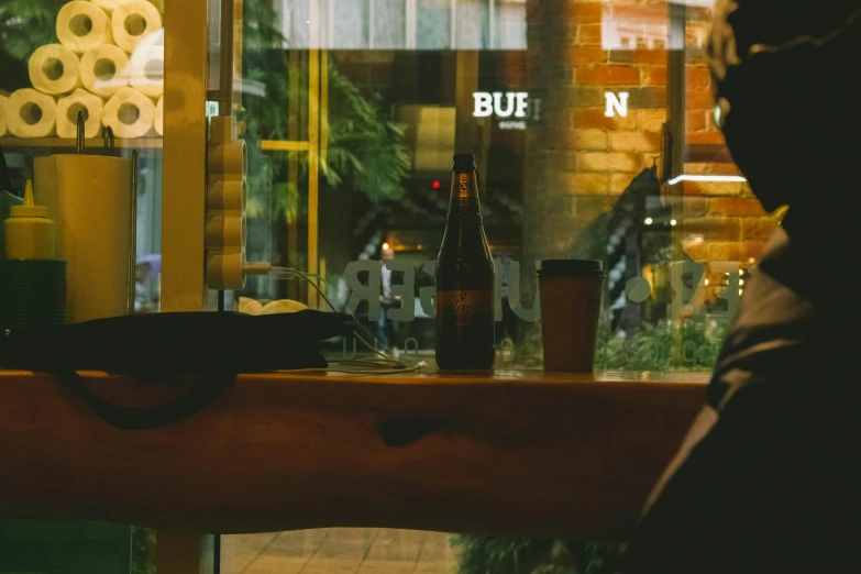 a person sitting at a table in front of a window, by Niko Henrichon, unsplash contest winner, a pint of beer sitting on a bar, blues, nighthawks, cold brew coffee )