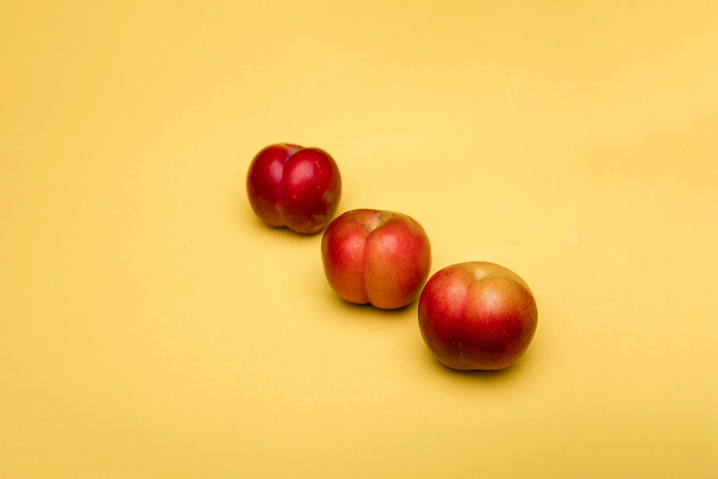 three apples sitting next to each other on a yellow surface, by Alison Geissler, unsplash, cherry, a human-like juicy peach, 15081959 21121991 01012000 4k, shot with sony alpha 1 camera