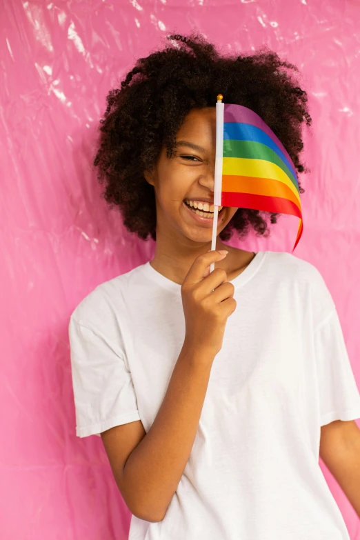 a young girl holding a rainbow flag in front of a pink wall, trending on unsplash, dark short curly hair smiling, teenage boy, with a white background, promo image