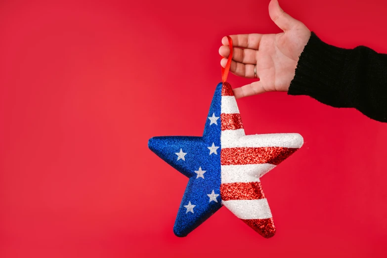 a person holding a red, white and blue star ornament, by Julia Pishtar, pexels, american realism, on a red background, 🚿🗝📝, uncle sam, on a canva