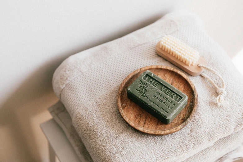 a soap bar sitting on top of a wooden plate, a still life, trending on pexels, olive green, lined in cotton, bath like style, jamie hewlet