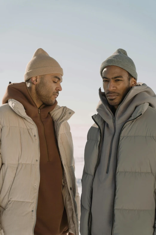 two men standing next to each other in the snow, trending on pexels, model wears a puffer jacket, light-brown skin, ( ( theatrical ) ), grey