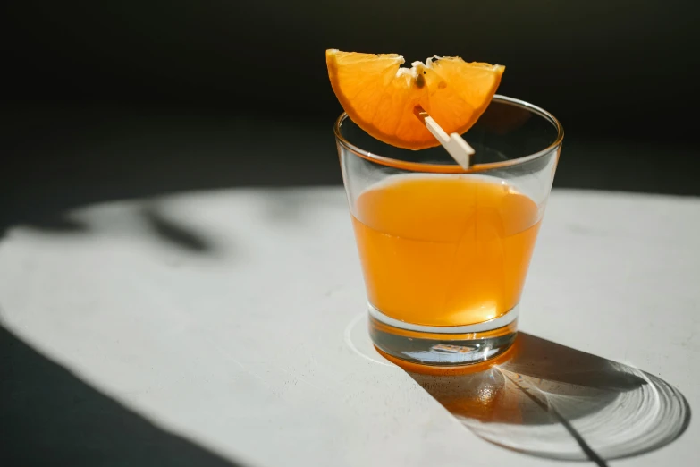 a glass of orange juice sitting on top of a table, a portrait, unsplash, drinks bourbon, grey orange, striking pose, midday light