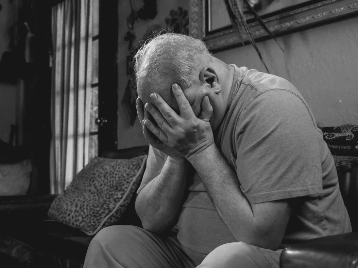 a man sitting on a couch with his head in his hands, a black and white photo, pexels, renaissance, nursing home, people crying, a photo of a man, florida man