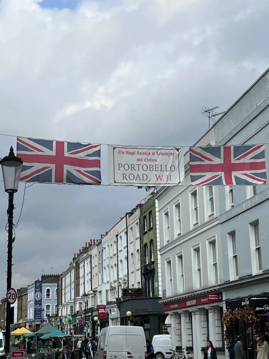 a crowd of people walking down a street next to tall buildings, inspired by Prince Hoare, reddit, united kingdom flags, shop front, regency-era, barnet