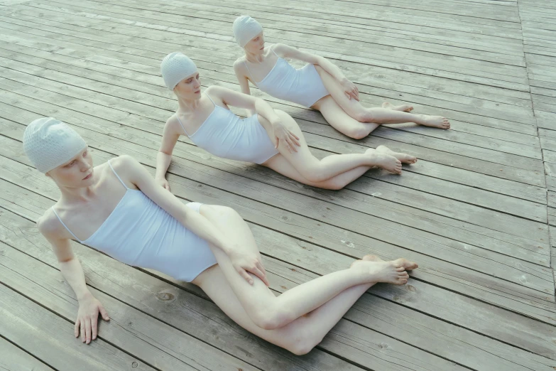 a couple of women sitting on top of a wooden floor, an album cover, inspired by Vanessa Beecroft, unsplash, fantastic realism, swimming, intense albino, 3 heads, wearing a white bathing cap