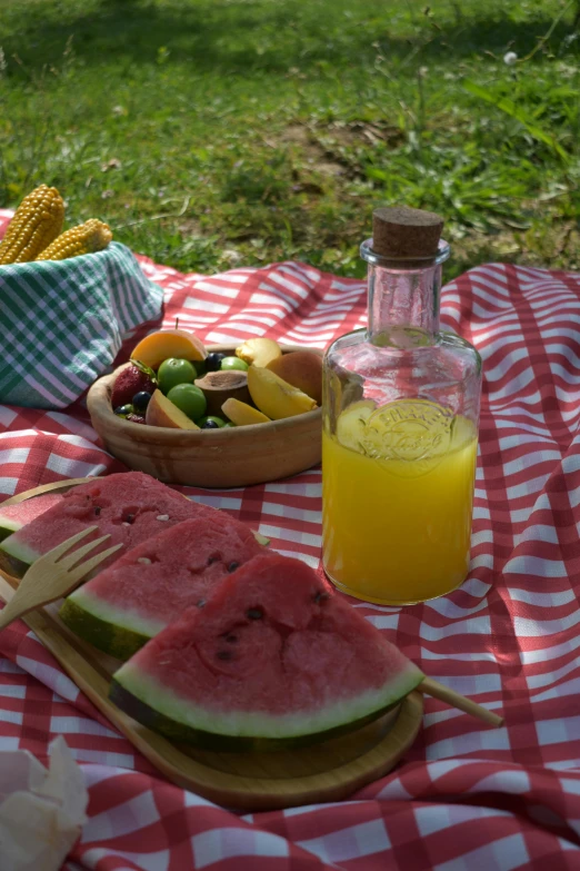 a picnic table with watermelon, corn and orange juice, holding a bottle, square, linen, no crop