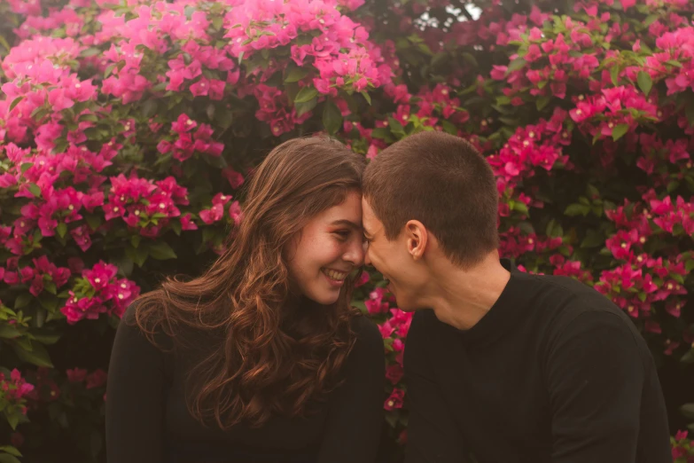 a man and woman standing next to each other in front of flowers, by Julia Pishtar, pexels contest winner, teen girl, smiling :: attractive, profile image, bougainvillea