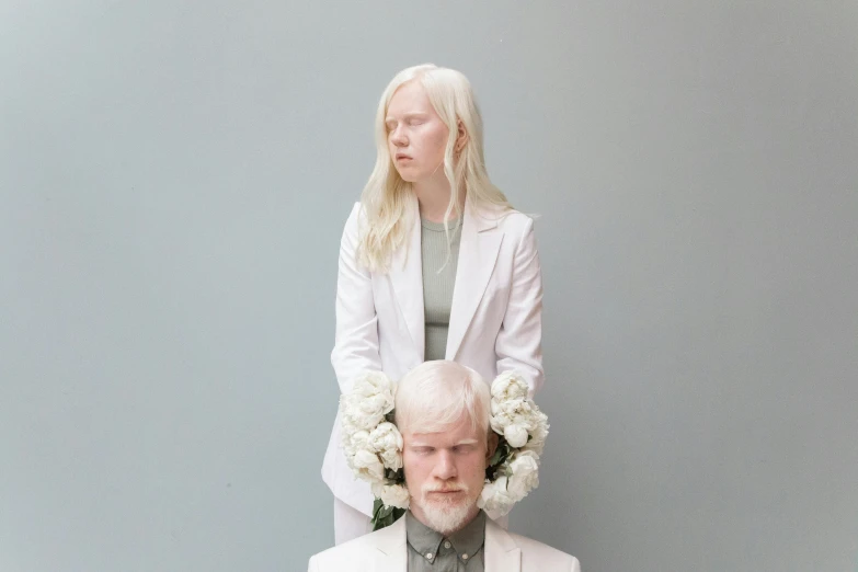 a woman sitting on top of a man's head, an album cover, by Louisa Matthíasdóttir, albino white pale skin, white flowers, wearing white suit, on a gray background
