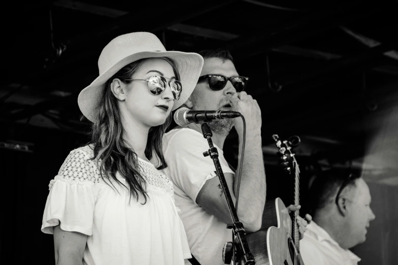 a couple of people that are standing in front of a microphone, a black and white photo, by Lee Loughridge, red sunglasses and a guitar, linsey levendall, summertime, scarlett hooft