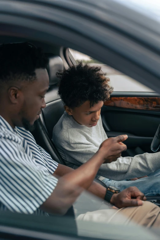 a man and a little boy sitting in a car, looking at his phone, square, black teenage boy, sharp focus »