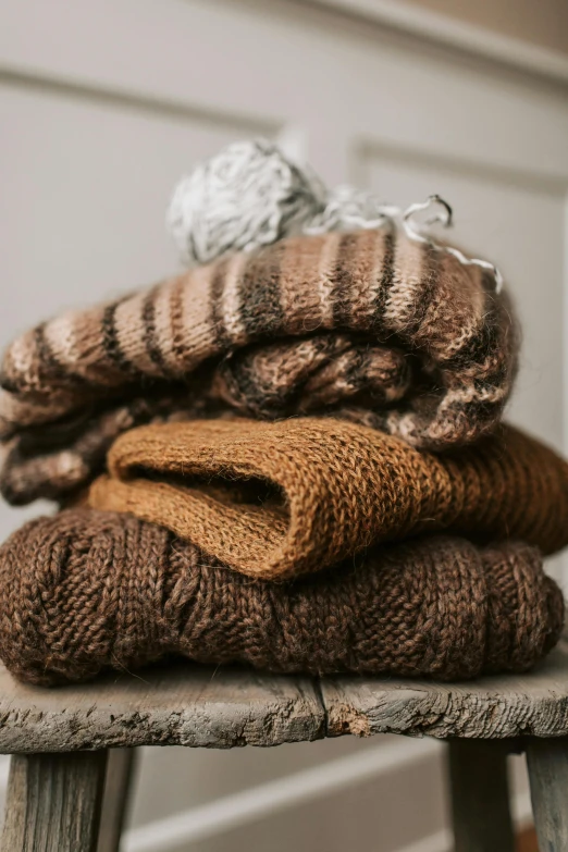 a stack of sweaters sitting on top of a wooden stool, by Jessie Algie, unsplash, brown color palette, caramel. rugged, chocolate, game ready