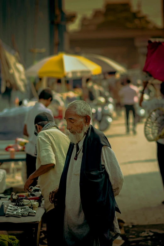 a group of people walking down a street with umbrellas, long white beard, on an indian street, paul barson, market stalls